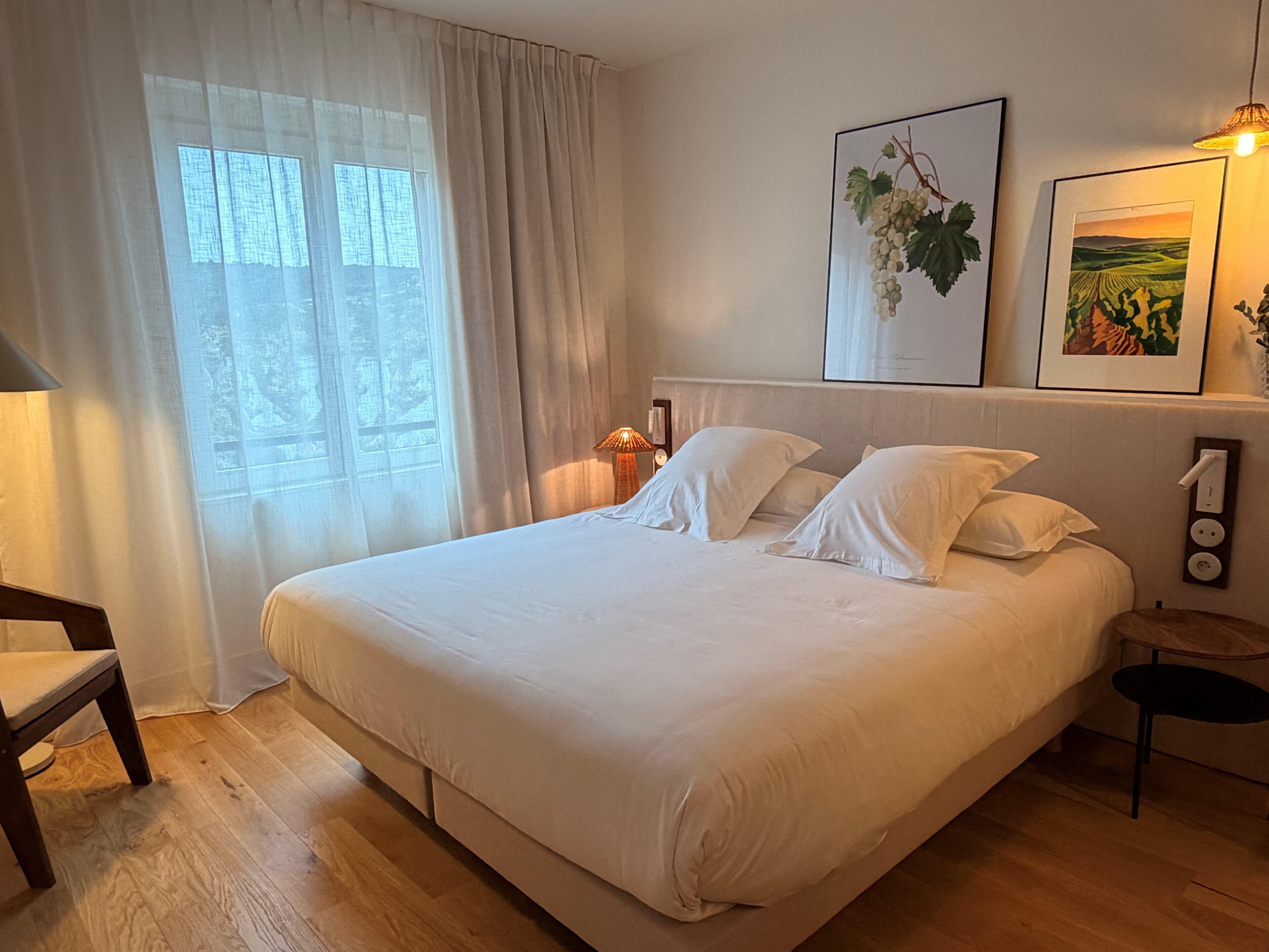 Un lit bien fait, avec du linge de lit blanc, une table de chevet avec une lampe et un tableau encadré au mur.