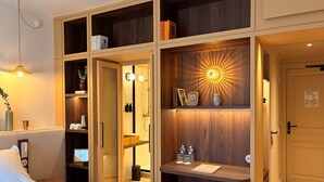 A hotel room with a bed, a desk with a chair, a vanity with a mirror, and a wardrobe with multiple shelves. - Le Beau Rivage (Condrieu)