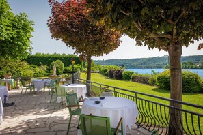 An outdoor patio with round tables and chairs, overlooking a lake and hills.