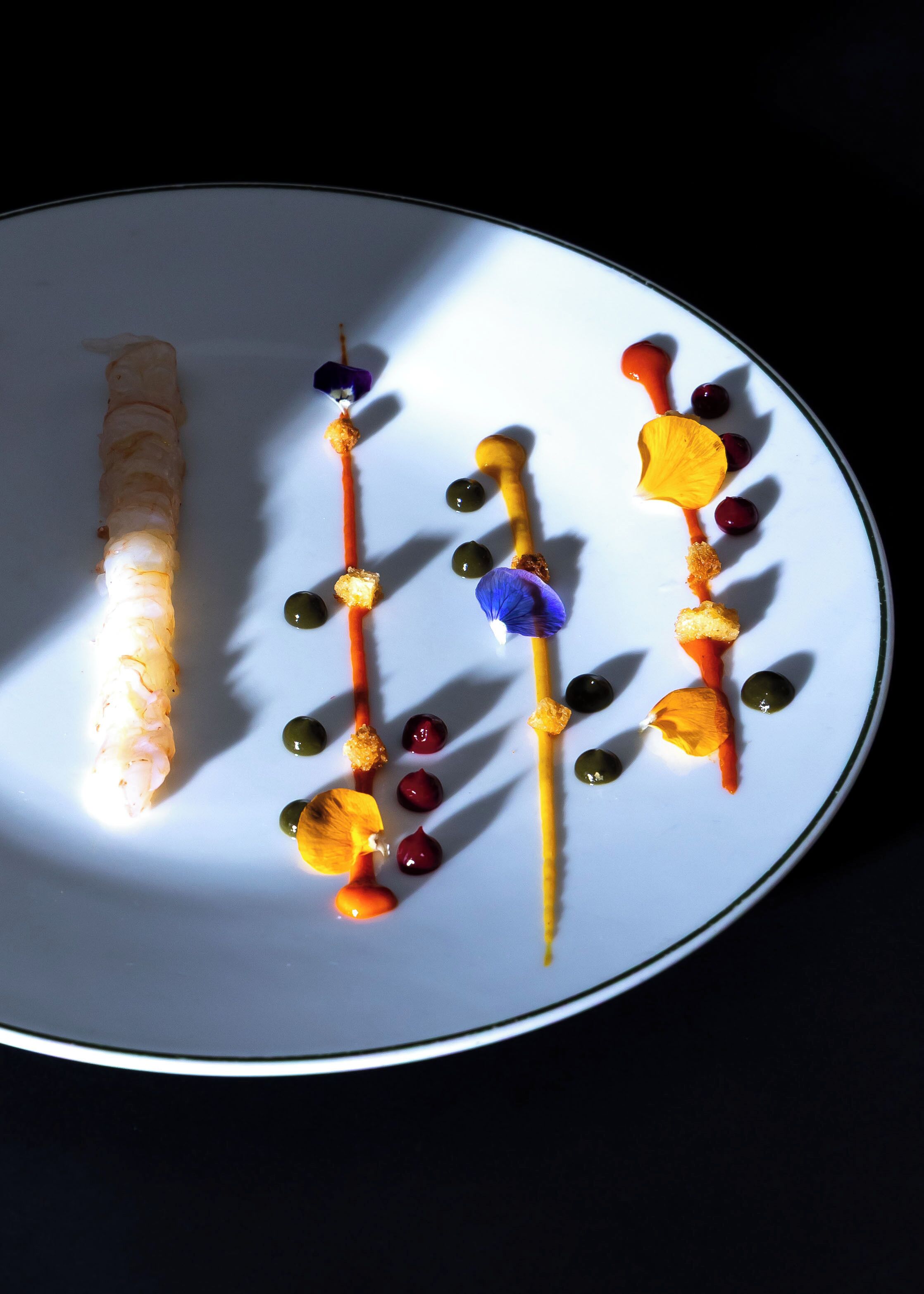 A white plate with a variety of food items, including a long, cylindrical piece of food, possibly a sushi roll, and several small, colorful garnishes.