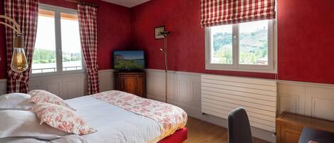A bedroom with a bed, a desk, a chair, a lamp, and two windows with curtains.
