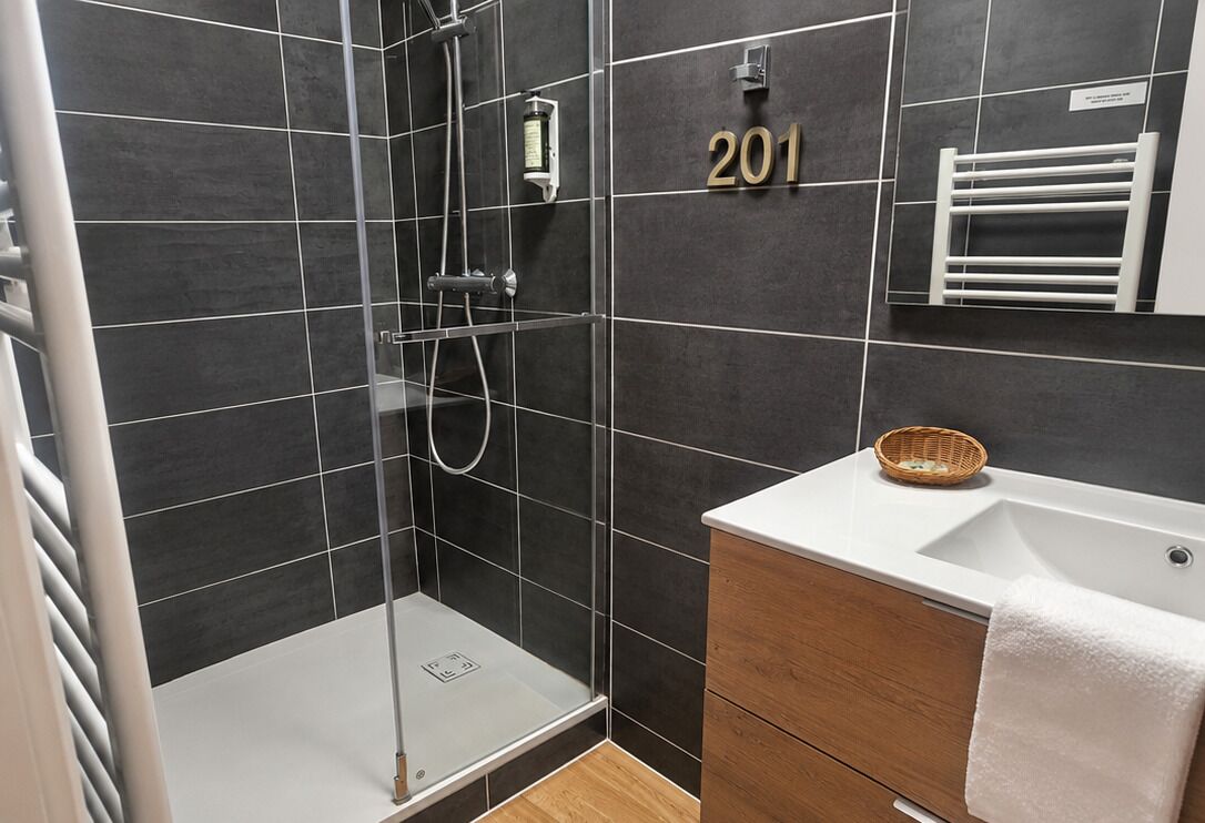 Een moderne badkamer met een douchecabine van glas, een witte wastafel en een meubel met een handdoek.