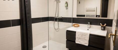 Un baño con ducha de vidrio, un lavabo con una toalla y un espejo.