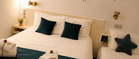 Habitación de hotel con dos camas, cada una con cubrecama blanco y verde azulado, almohadas y toallas. Se observan elementos decorativos en la pared y una mesita de noche con lámpara.