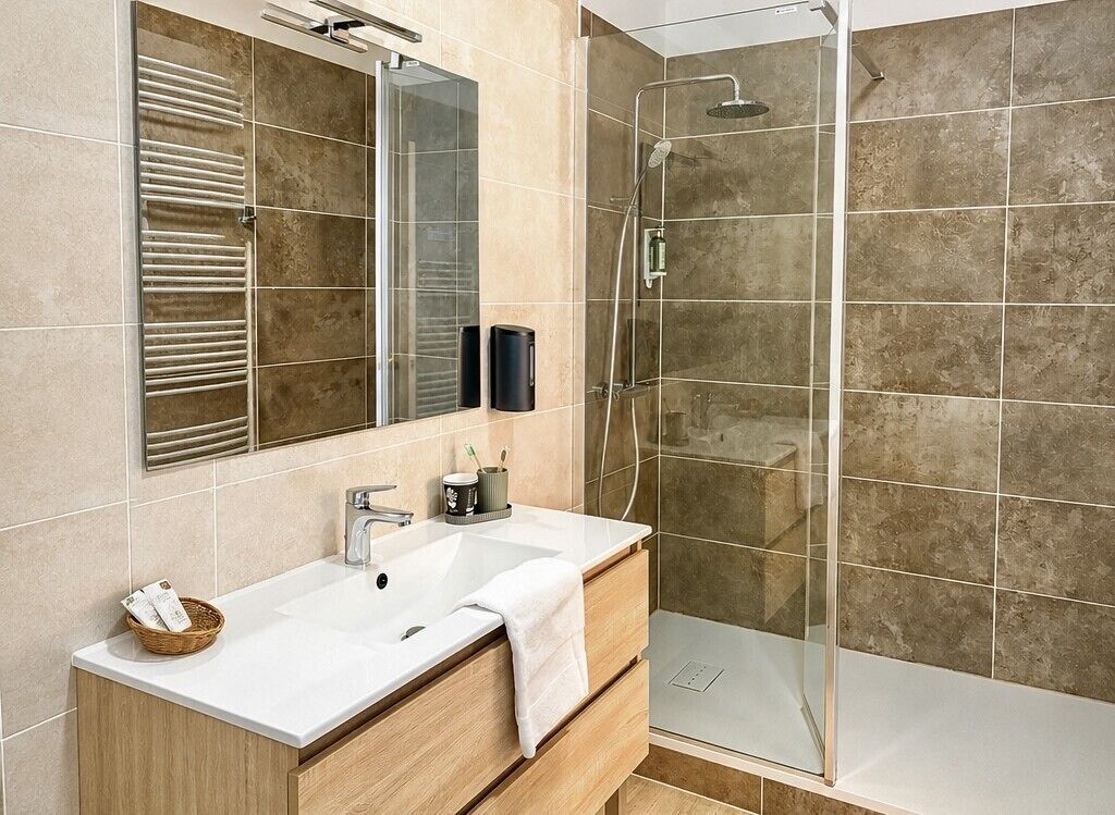 A modern bathroom with a glass shower enclosure, a white sink with a wooden vanity, and a large mirror.