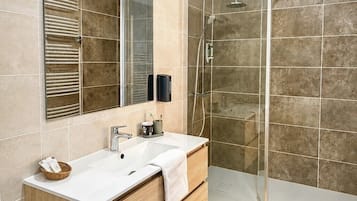 A modern bathroom with a glass shower enclosure, a white sink with a wooden vanity, and a large mirror.