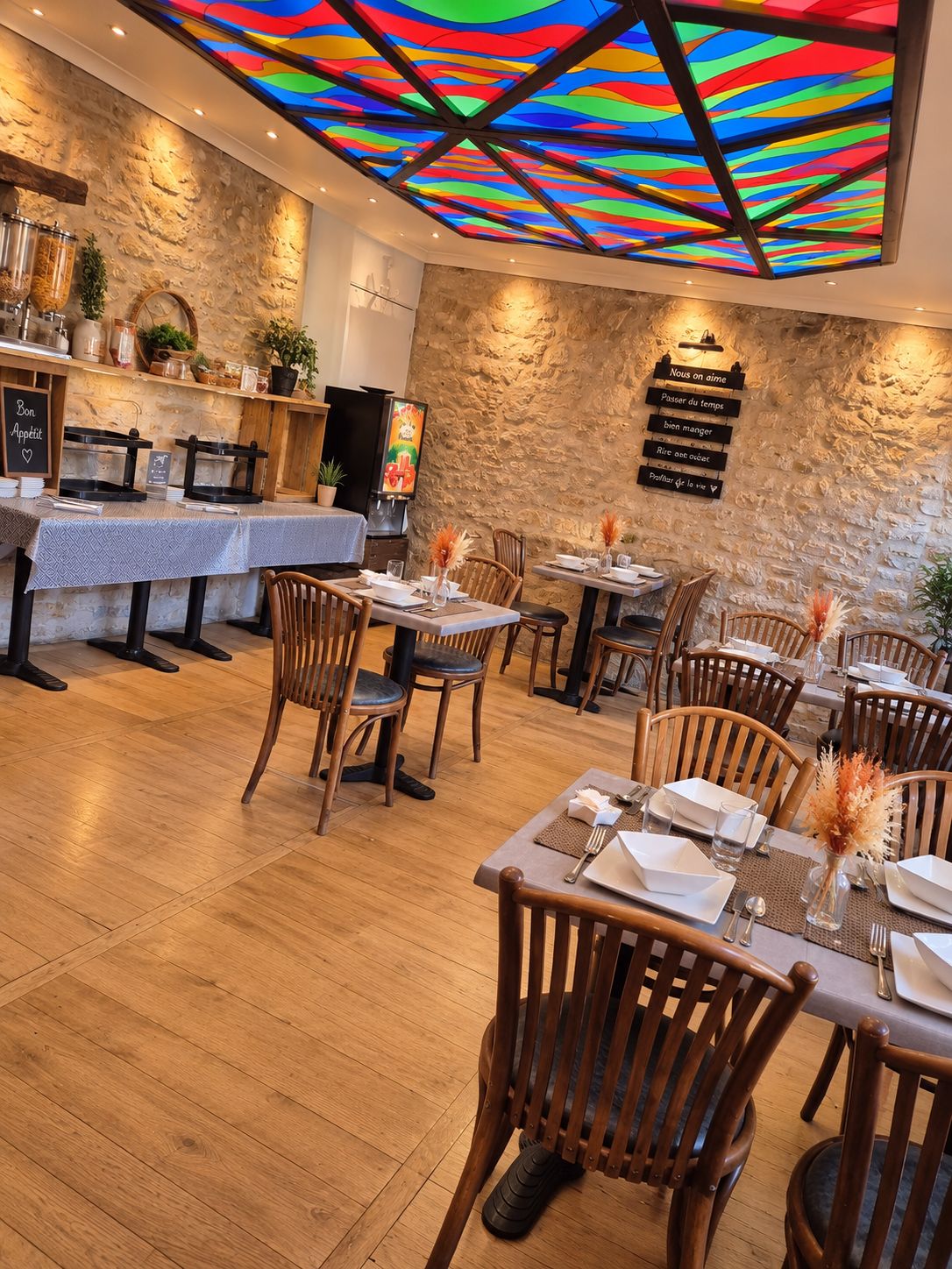 Ein Restaurantinneres mit Holzboden, gedeckten Tischen und einem farbenfrohen Deckengestaltung.