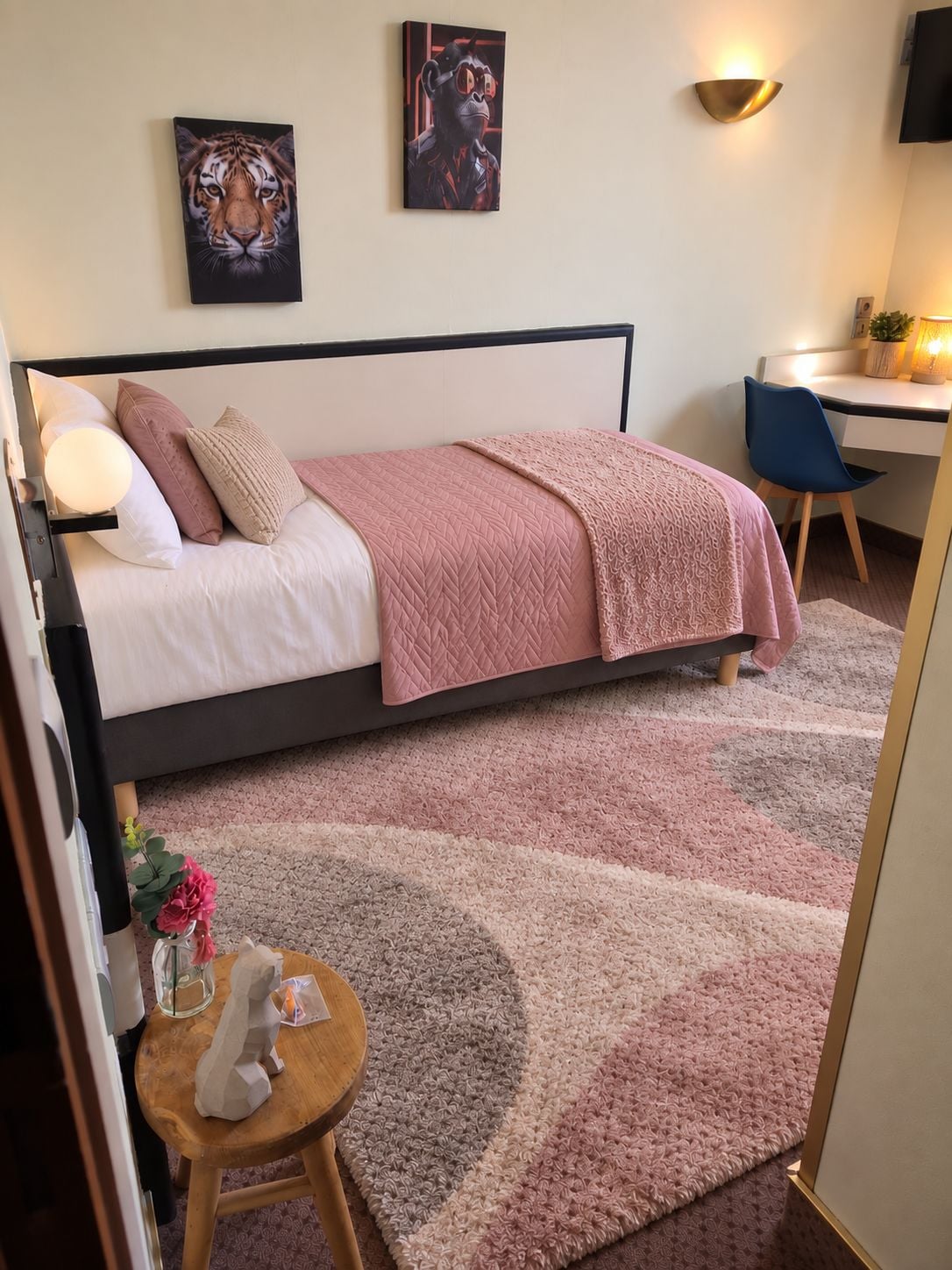 A bedroom with a bed, a desk, a chair, a lamp, and a wall-mounted TV.