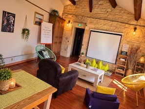 A cozy room with a stone wall, a whiteboard, a projector screen, and comfortable seating. - Le Lion d'Or (Gramat)