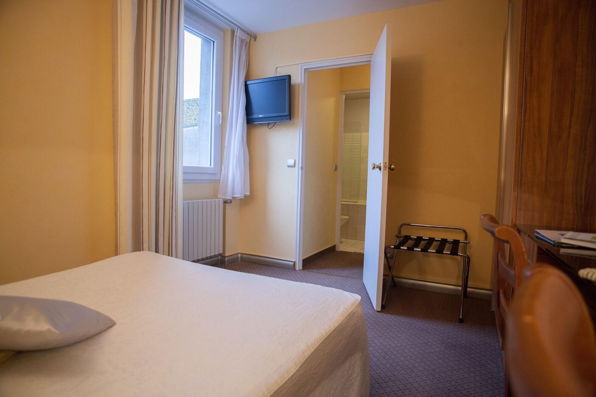 A hotel room with a bed, a TV, a bathroom door, and a towel rack.