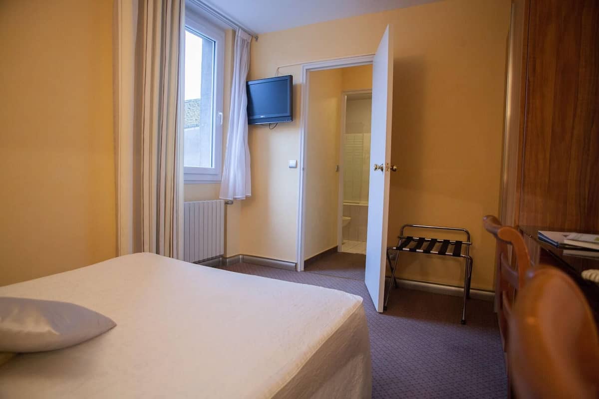 Quarto de hotel com uma cama, televisão, porta do banheiro e porta-toalhas.