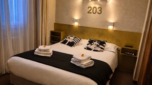 A hotel room with a large bed, two nightstands, a wall-mounted number sign, and a window with curtains.