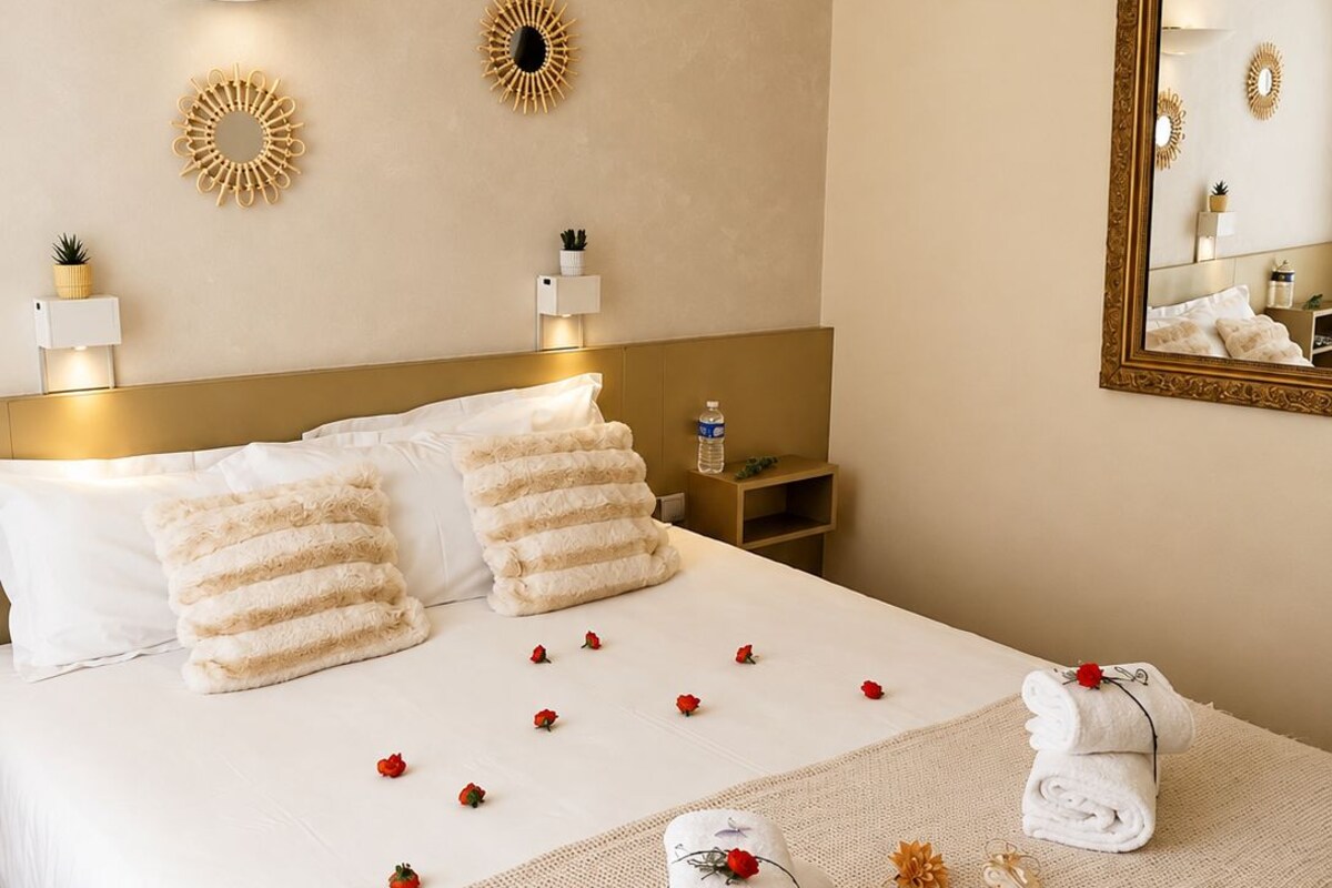 A hotel room with a large bed, two wall sconces, a mirror, and decorative wall art.
