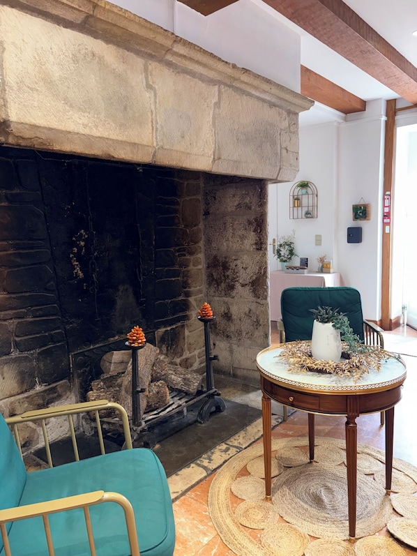 A cozy living room with a fireplace, a teal armchair, a wooden coffee table with a decorative centerpiece, and a green chair. - Le Lion d'Or (Gramat)