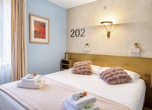 Habitación de hotel con cama, número de pared '202', un cuadro enmarco y una lámpara de noche.