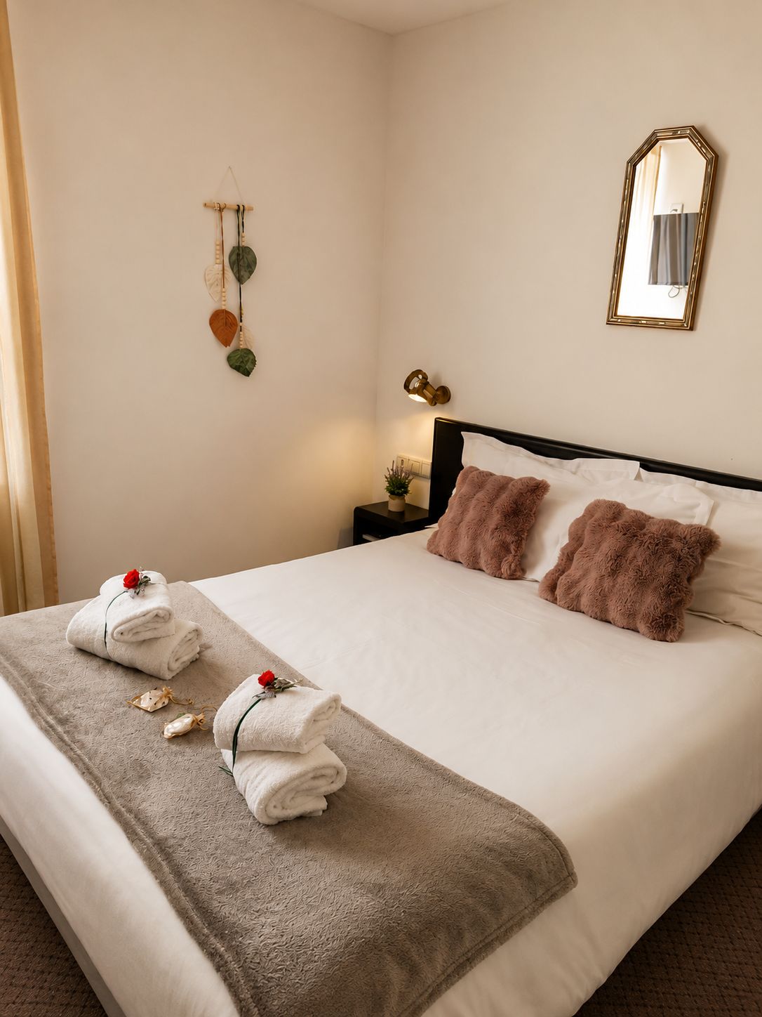 A neatly made bed with towels and a blanket, a bedside lamp, a wall-mounted mirror, and a wall decoration.