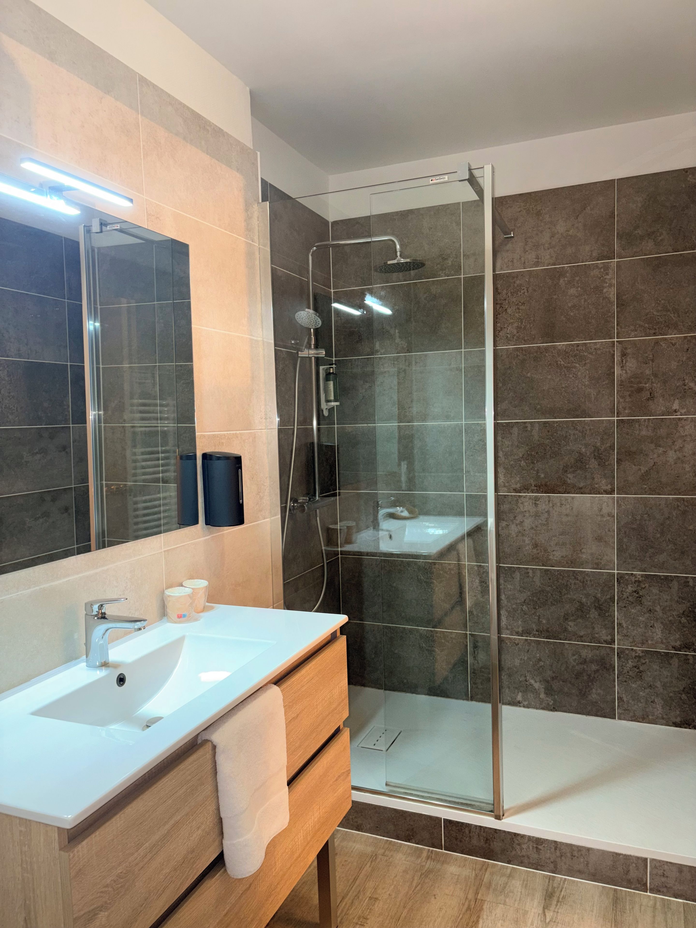 Un baño moderno con ducha de vidrio, lavamanos blanco y un espejo grande.