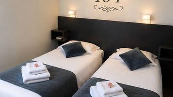 Habitación de hotel con dos camas, un letrero con número en la pared y una mesita de noche.