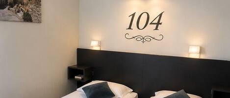 A hotel room with two beds, a wall-mounted number sign, and a nightstand.