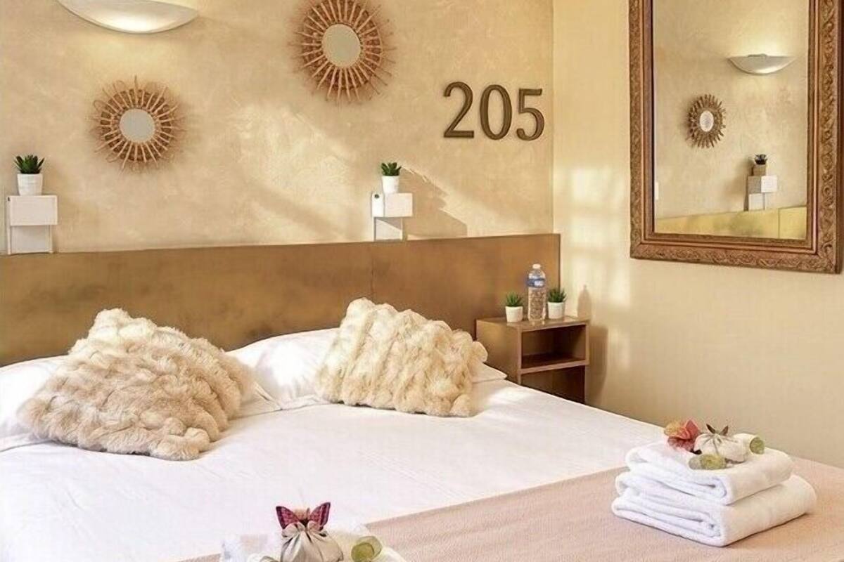 Quarto de hotel com uma cama grande, cabeceira, número de parede '205', um espelho e uma pequena prateleira com artigos de higiene pessoal.
