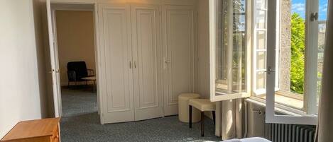 A bedroom with a bed, a bench, a wooden dresser, a wardrobe, and a window with a view.