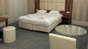 A hotel room with a bed, a round table, a chair, a desk, and a lamp.