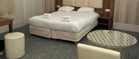 A hotel room with a bed, a round table, a chair, a desk, and a lamp.
