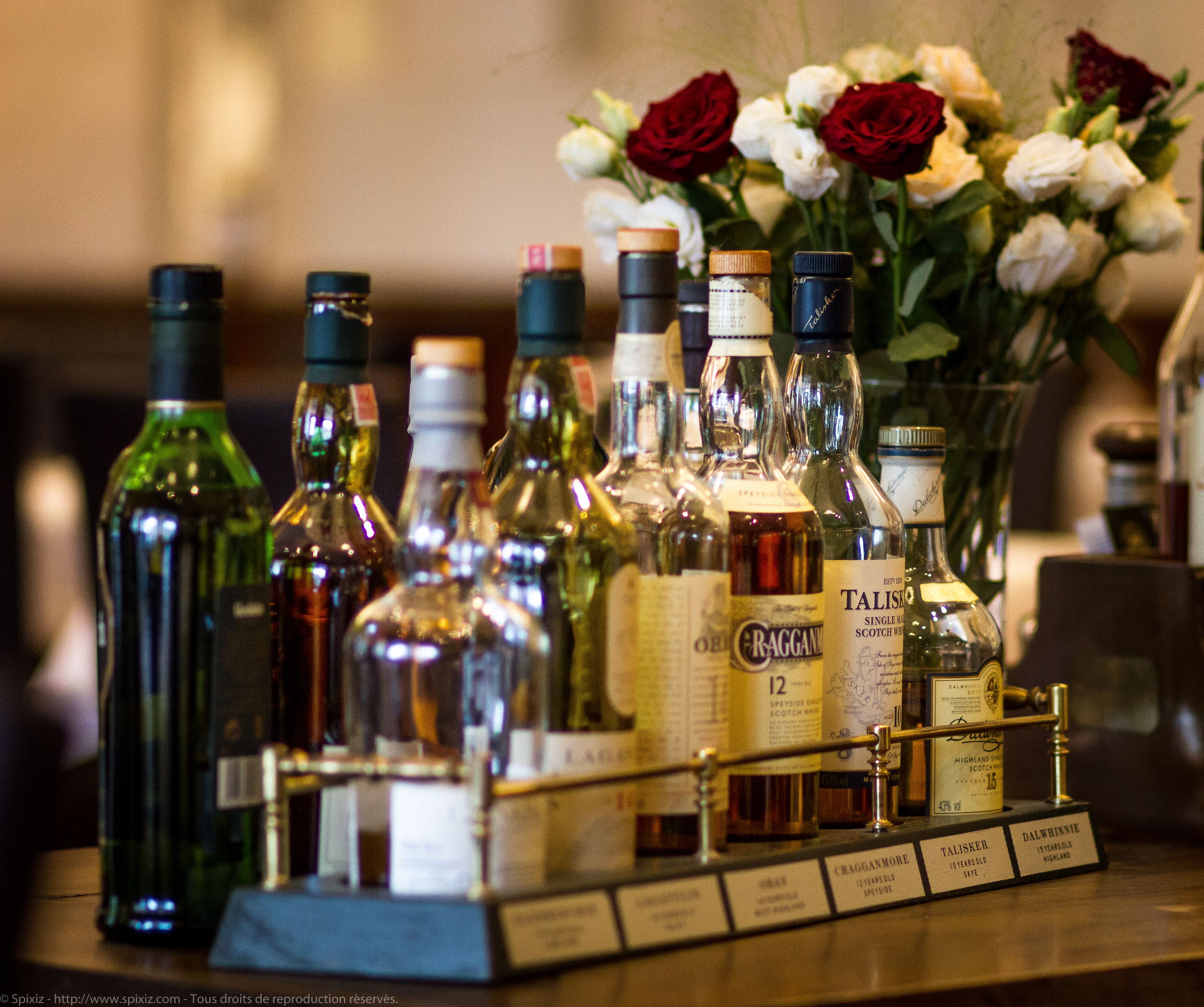 A bar area with various bottles of liquor, a flower arrangement, and a metal rack with labels.