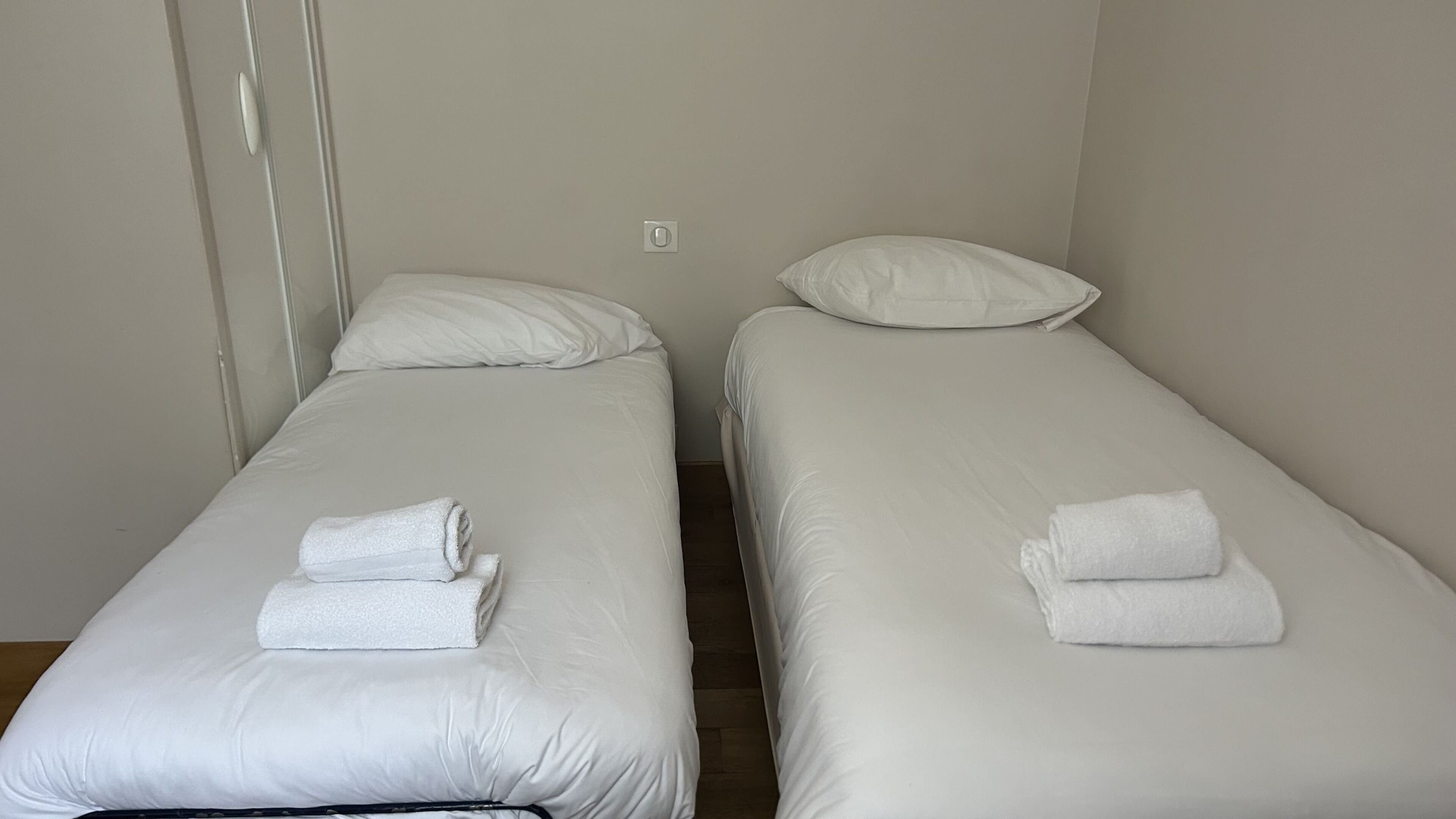 Two single beds with white linens and towels, a white wall, and a door.