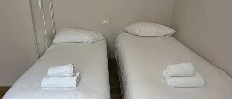 Two single beds with white linens and towels, a white wall, and a door.