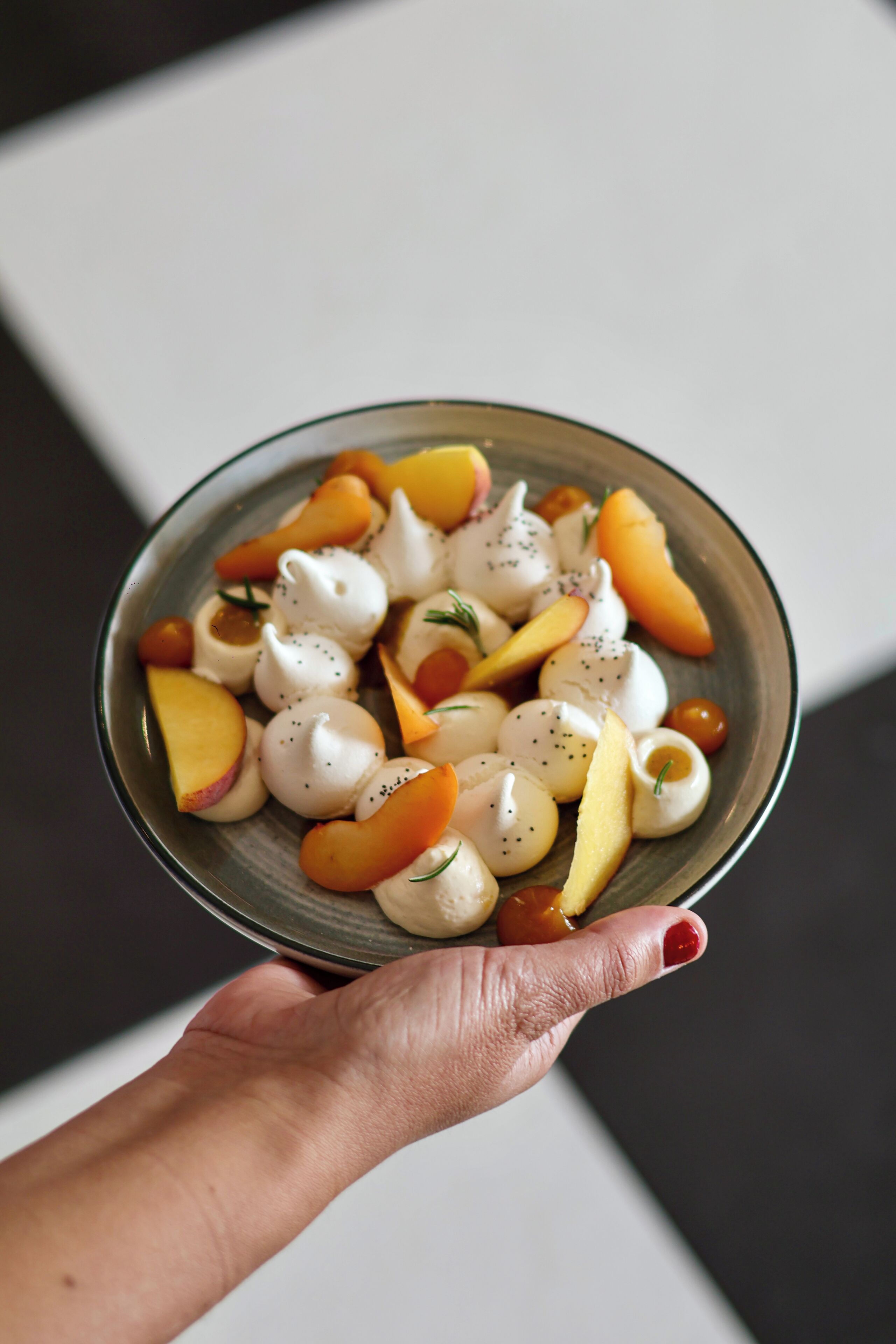 A hand holding a bowl of food with various fruits and a white creamy substance.