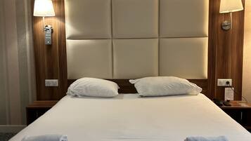 A hotel room with a large bed, two bedside lamps, a wooden headboard, and a wall with striped wallpaper.