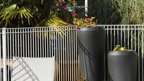 Una piscina con cerramiento metálico, sillas de descanso y macetas grandes.
