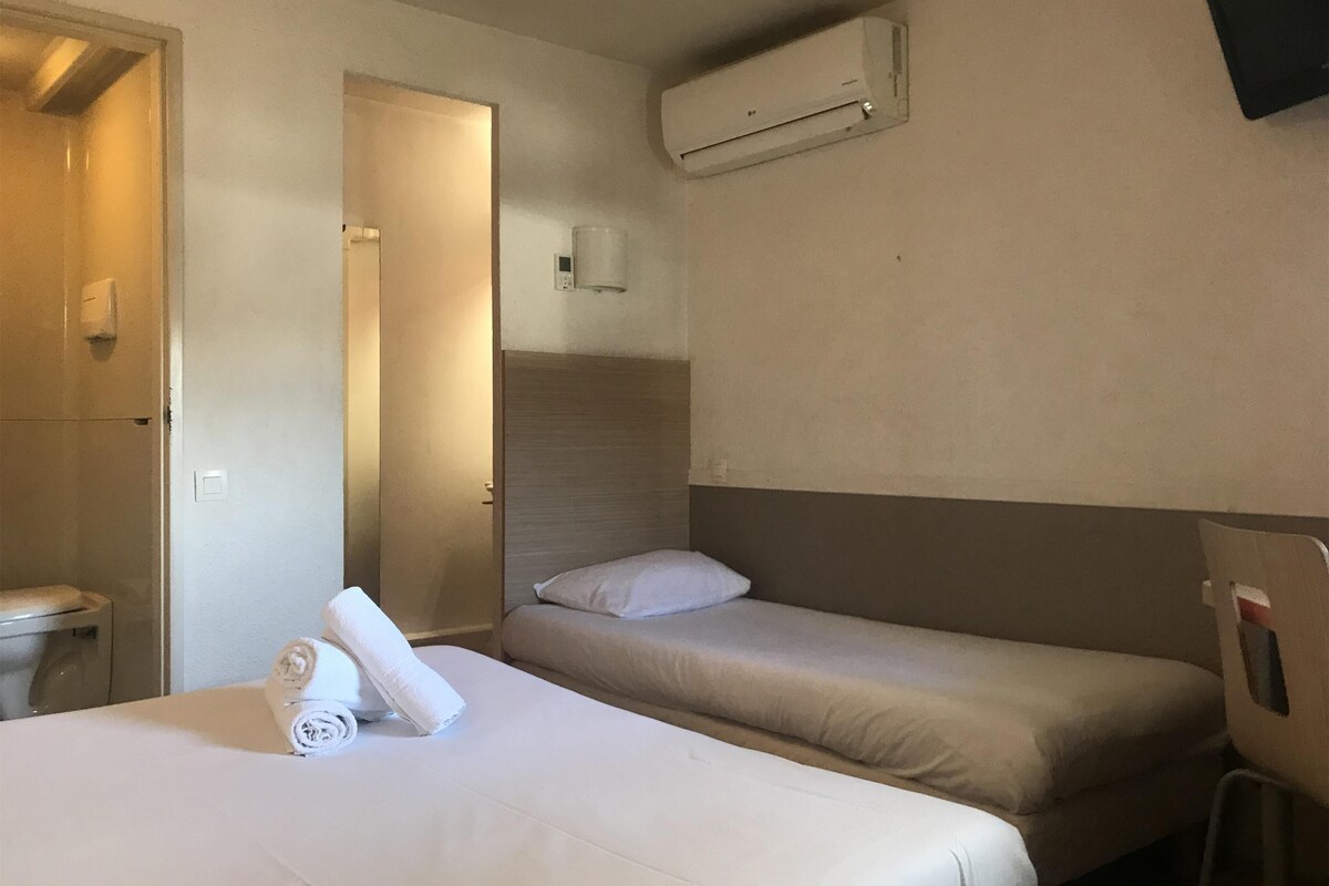 Habitación de hotel con dos camas, baño y aire acondicionado.