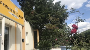 A hotel entrance with a yellow sign, a wheelchair-accessible entrance, and a garden with plants and a bench. - Premiere Classe Avignon Courtine (Avignon)