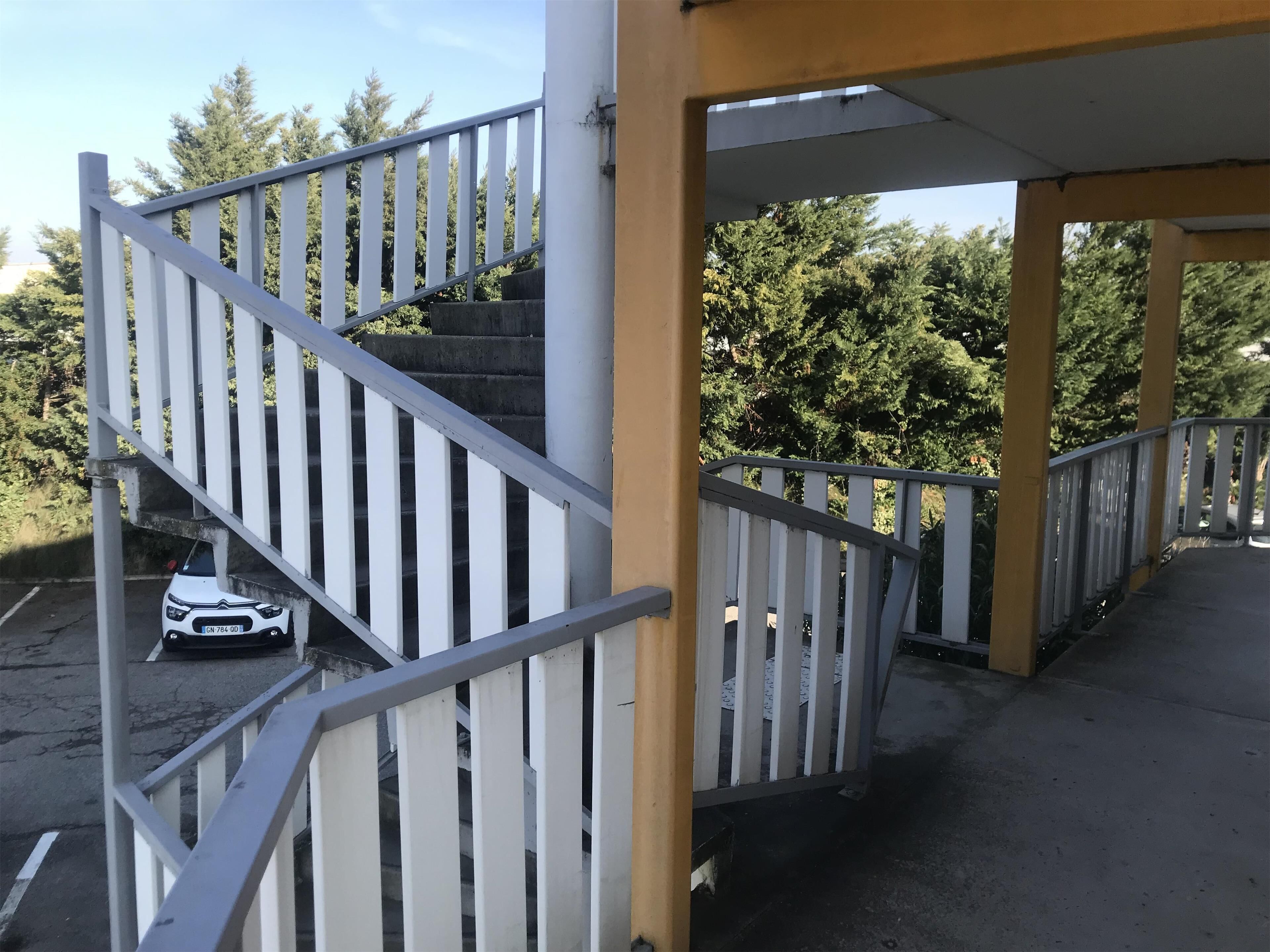A staircase with white railings leading to an upper level, surrounded by greenery.