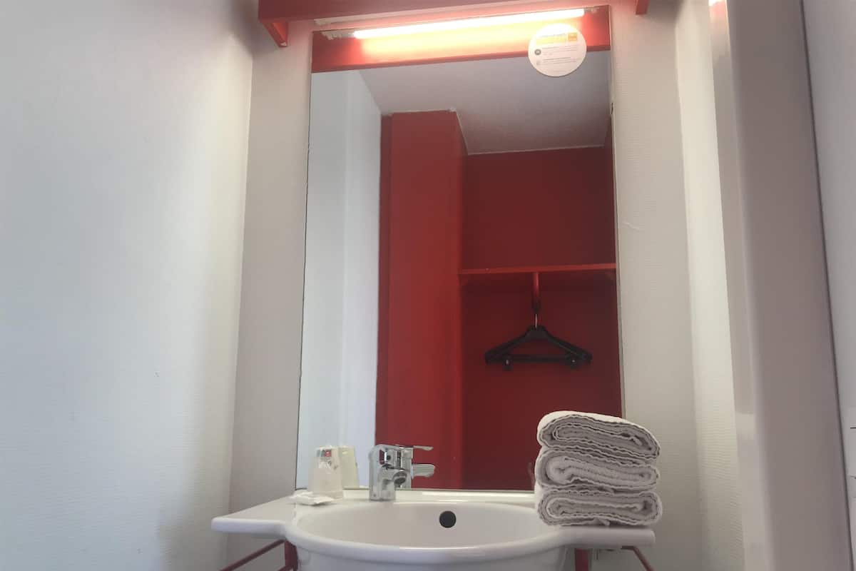 A bathroom with a white sink, a mirror, and a red towel rack.