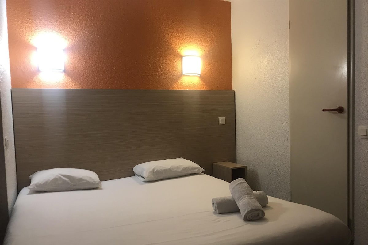 A hotel room with a bed, two pillows, a nightstand, a lamp, and a door.