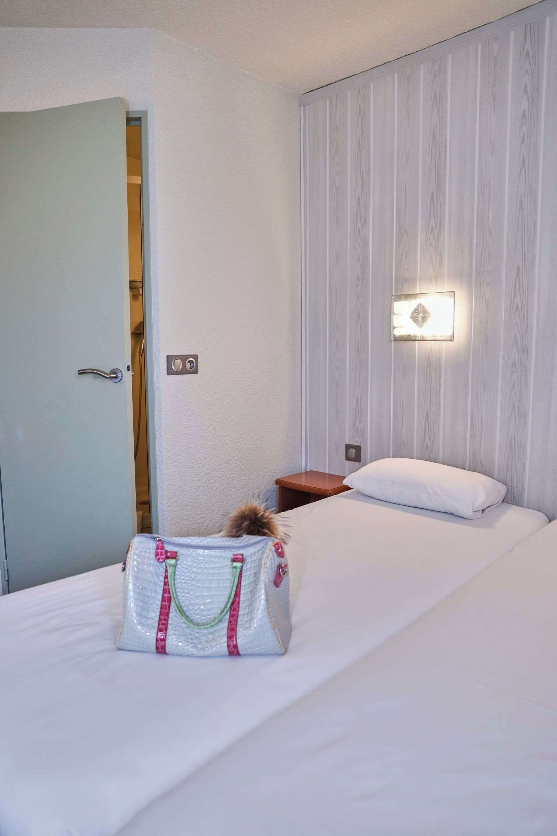Una habitación de hotel con una cama, una mesita de noche, una lámpara de pared y una puerta.