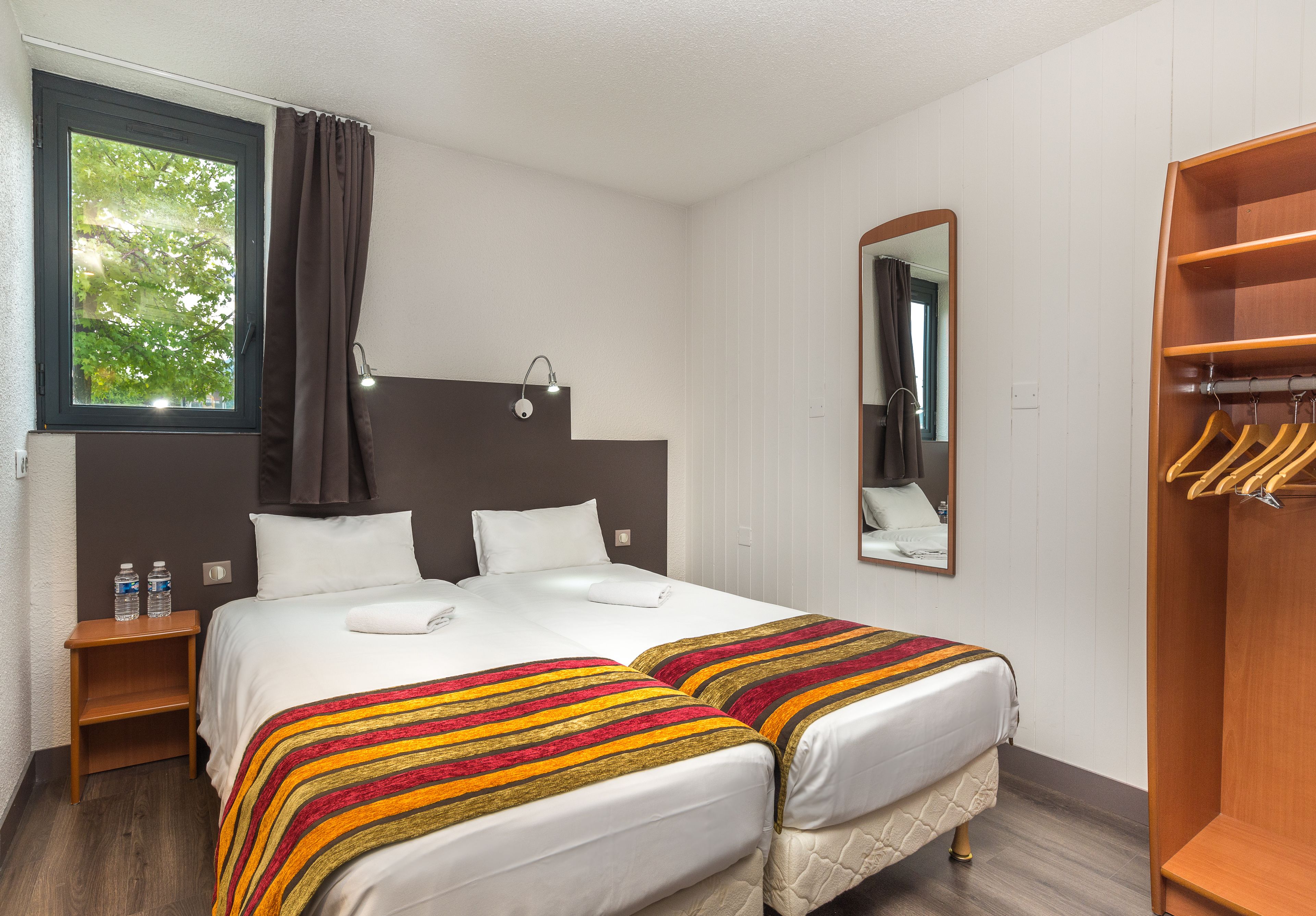 Habitació d'hotel amb un llit, dues taules de nit, un mirall, un armari i una finestra amb cortines.