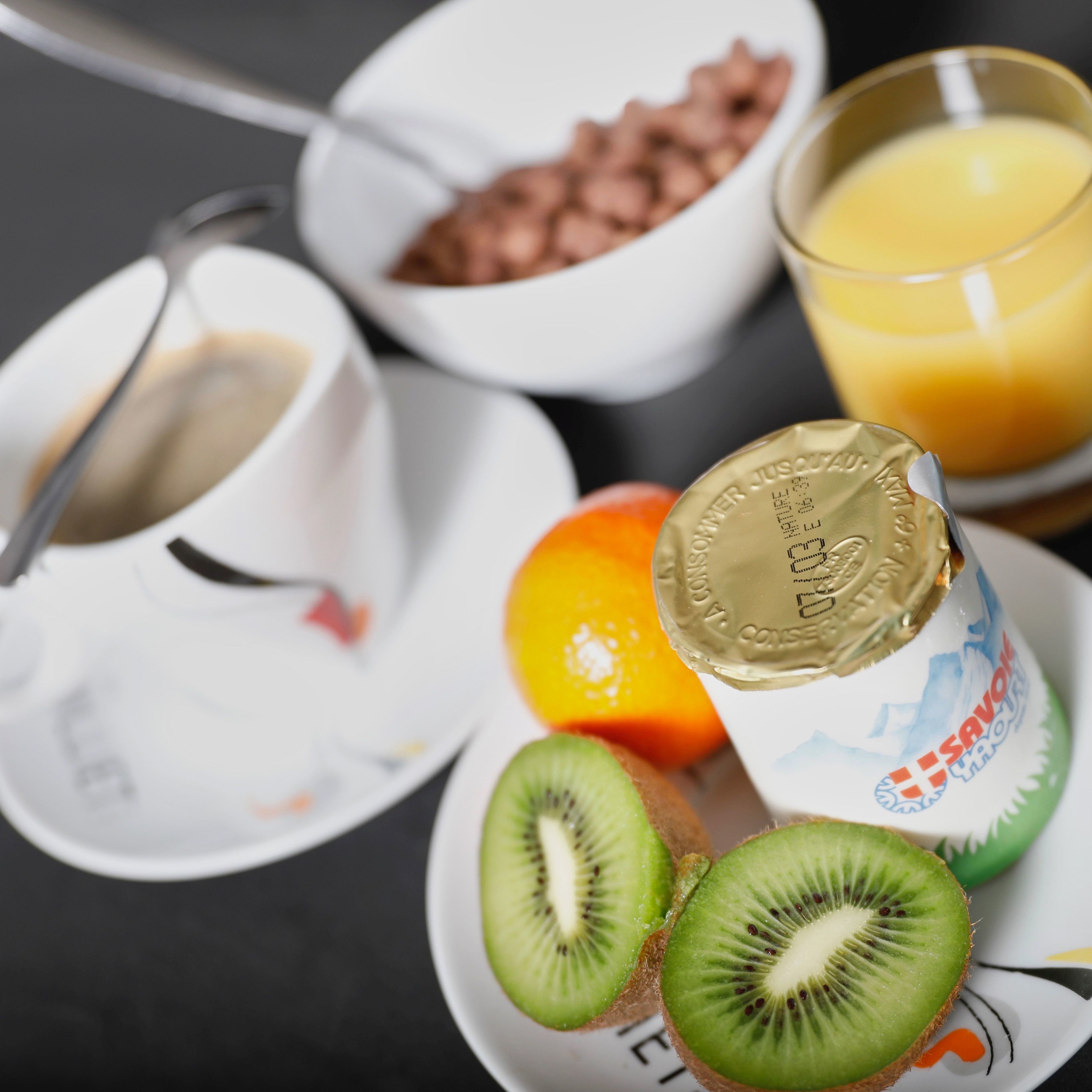 Desayuno con un tazón de cereal, un vaso de jugo de naranja, un vaso de leche y un tarro de yogur.