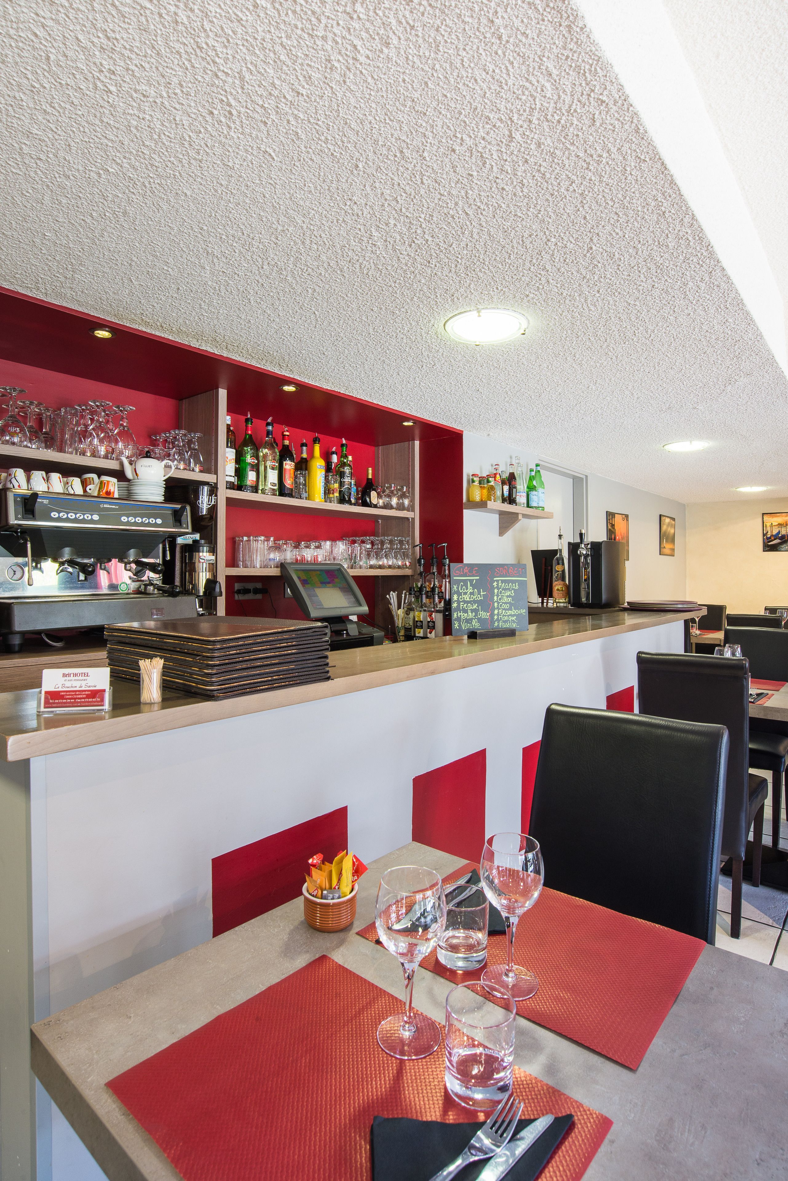 Eine Barbereich mit einer Kaffeemaschine, Regalen voller Flaschen, Gläsern und einer Speisekarte.