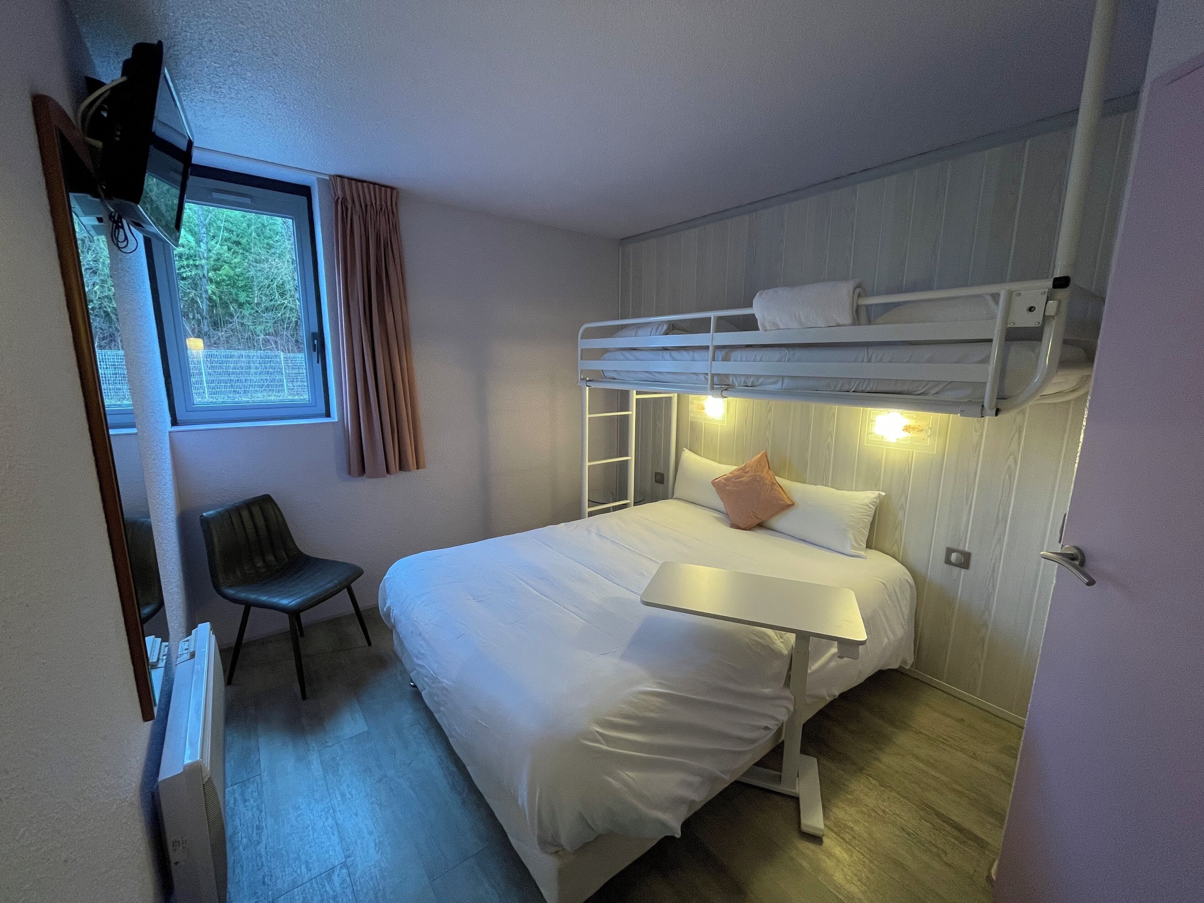 A bedroom with a bunk bed, a desk, a chair, and a window with curtains.