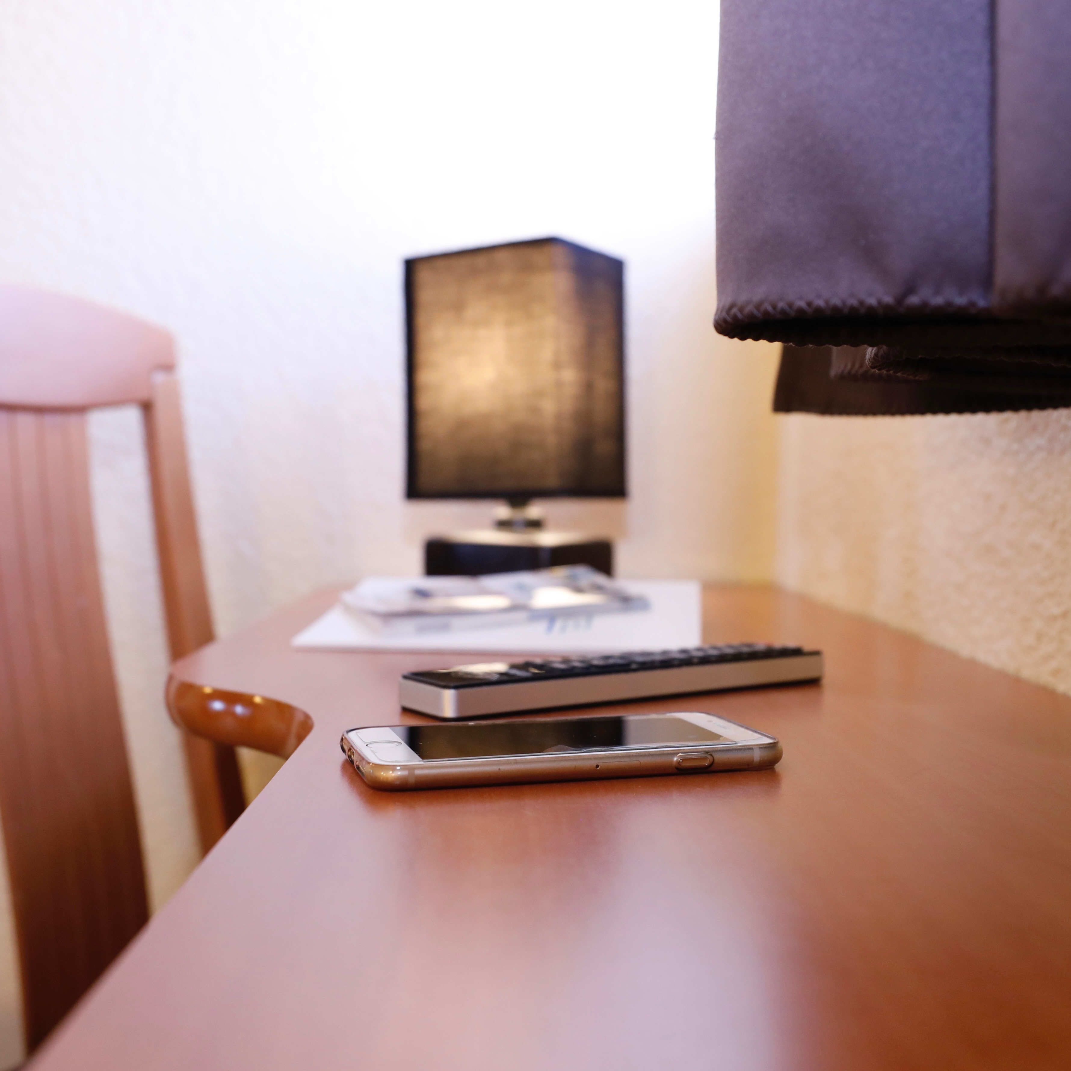 Una mesa de madera con un teléfono inteligente, un teclado y un monitor.