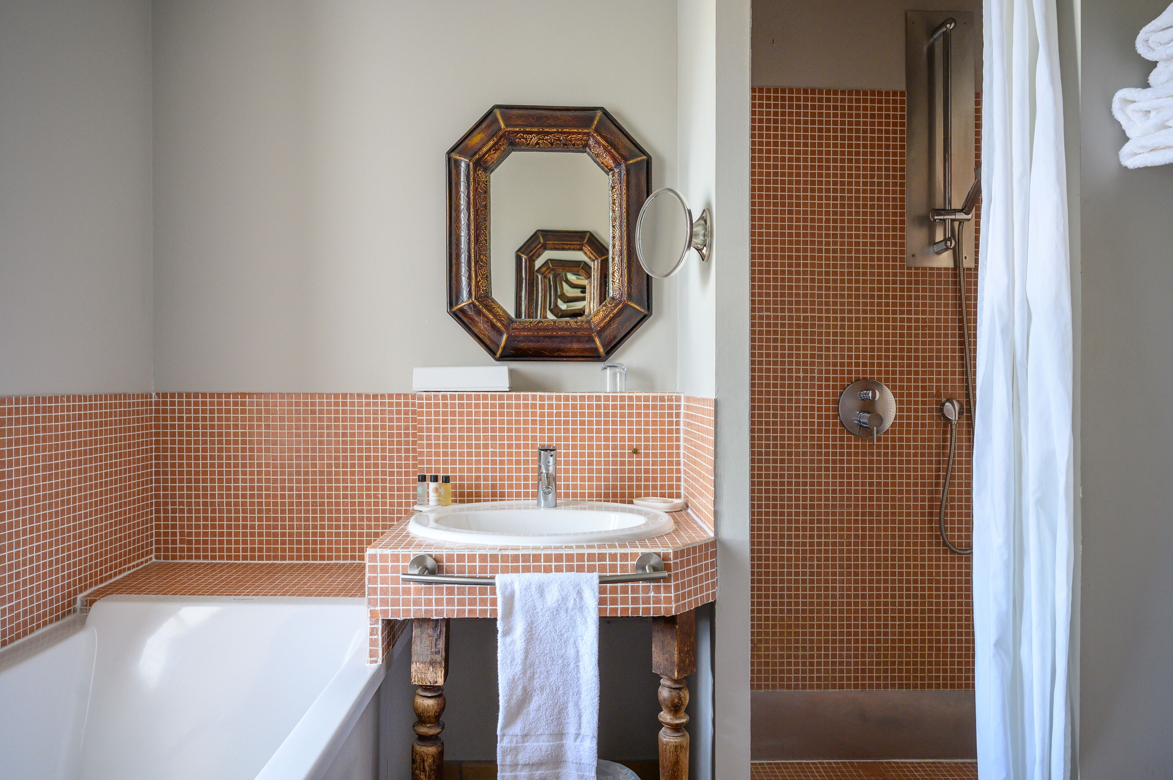 Une salle de bain avec une baignoire blanche, un lavabo avec un miroir au-dessus, et un espace douche séparé par un rideau.