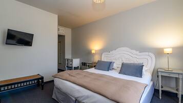 Habitación de hotel ordenada con cama, lámparas de noche, televisor y un banco.