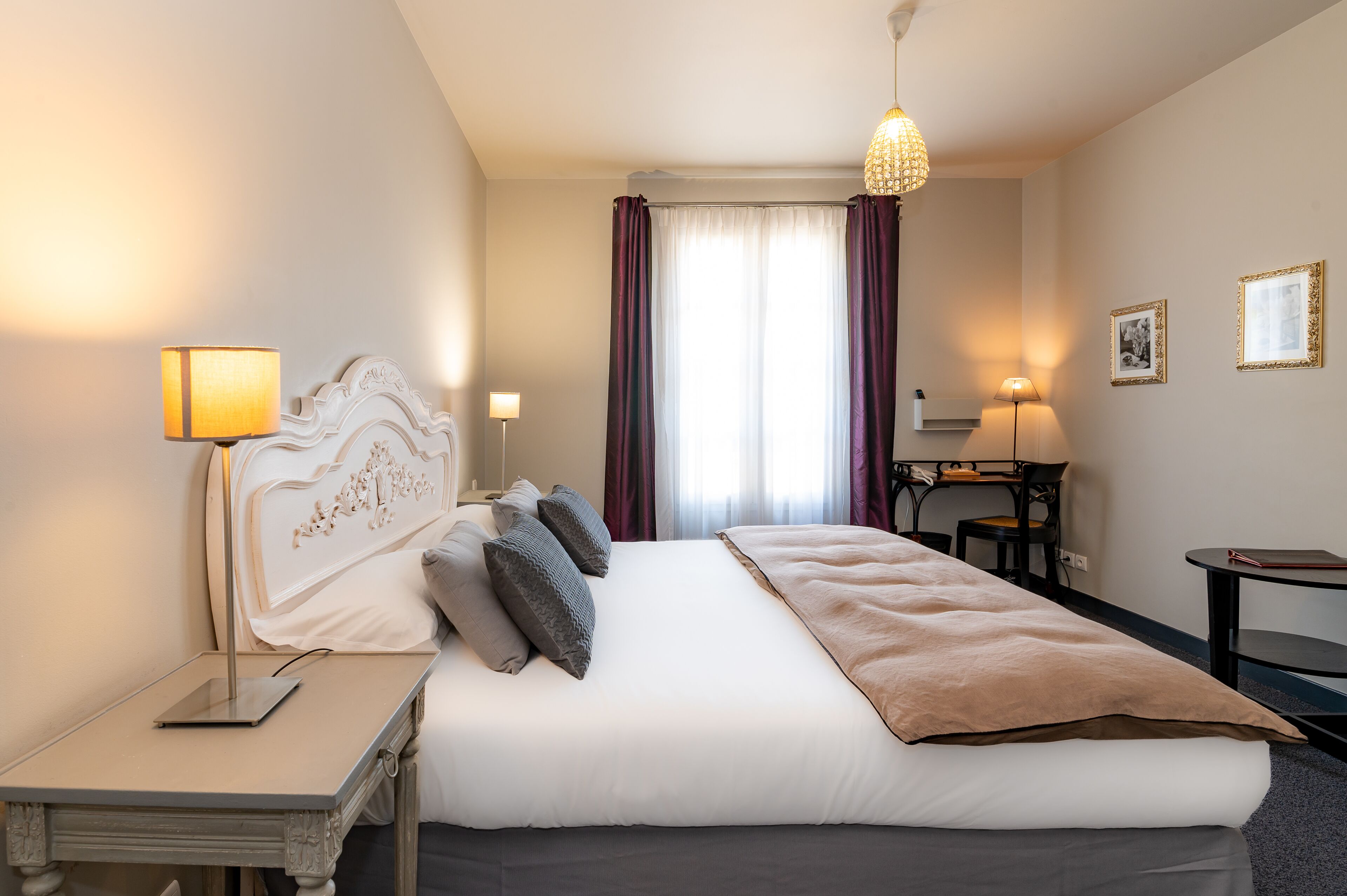 Una habitación de hotel ordenada con una cama grande, lámparas de noche, un escritorio y una silla.