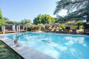 Una piscina con sillas de descanso y sombrillas, rodeada de follaje y árboles.
