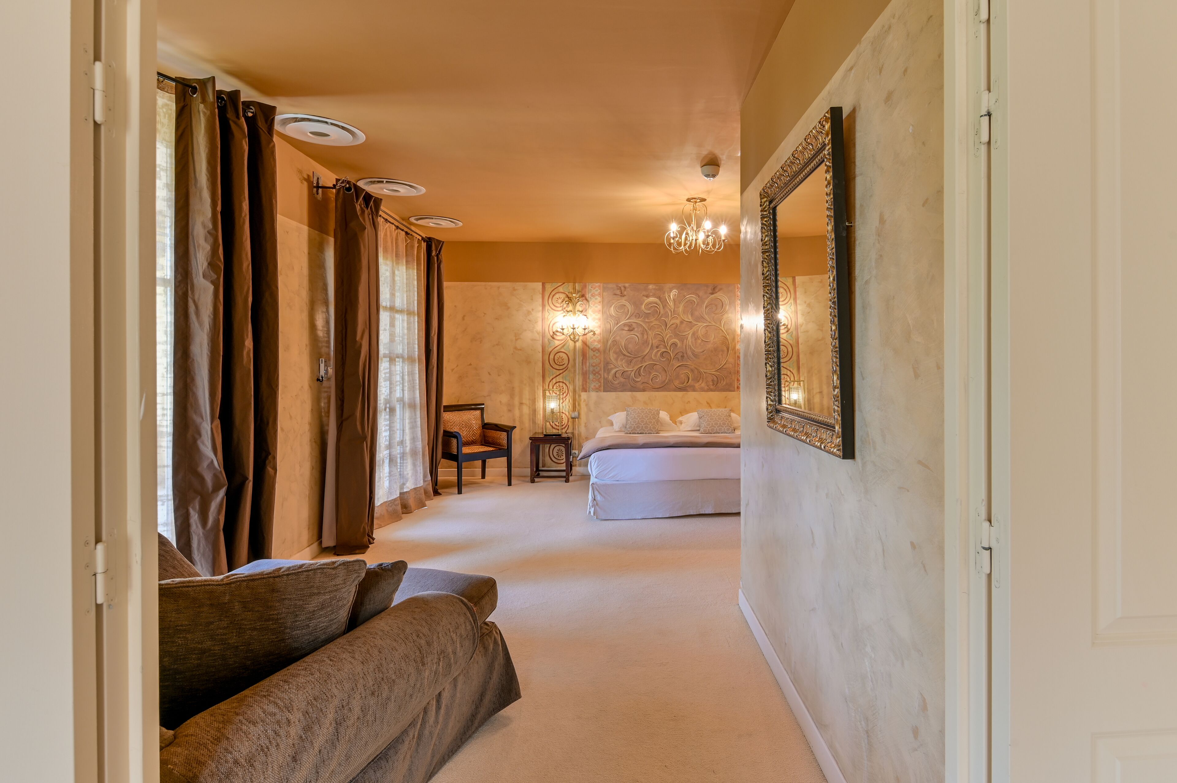 A hotel room with a bed, a sofa, a chair, and a chandelier.