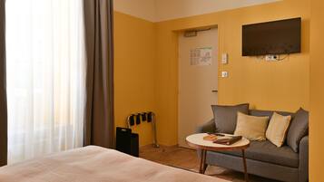 Quarto de hotel com cama, sofá, televisão fixada na parede e porta com mapa.
